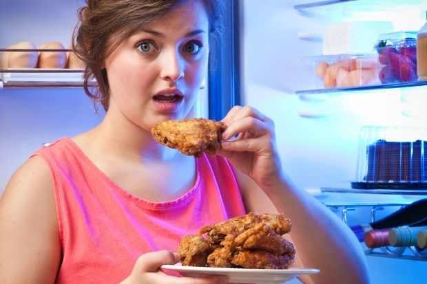 Woman eating cold chicken in front of the refrigerator