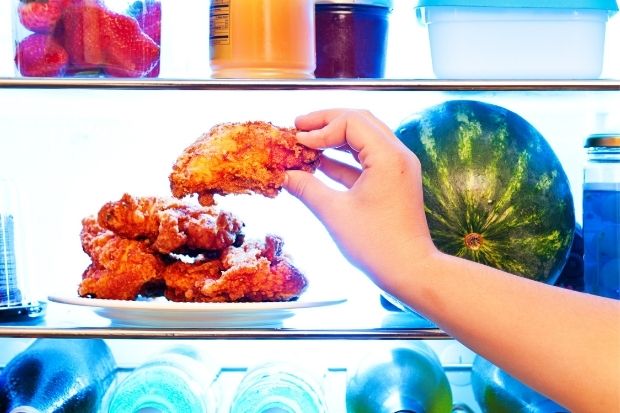 A hand takes cold chicken from the refrigerator to eat it
