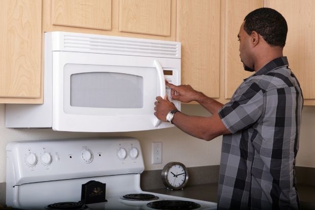 Man pressing button on microwave to reheat nachos