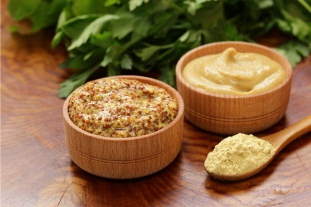 Two small containers of mustard, one with seeds and one without