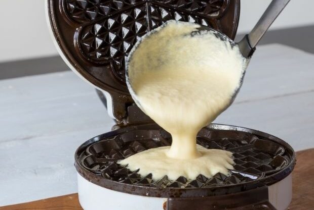 Waffle batter being poured onto waffle maker sparingly to prevent waffles splitting in half