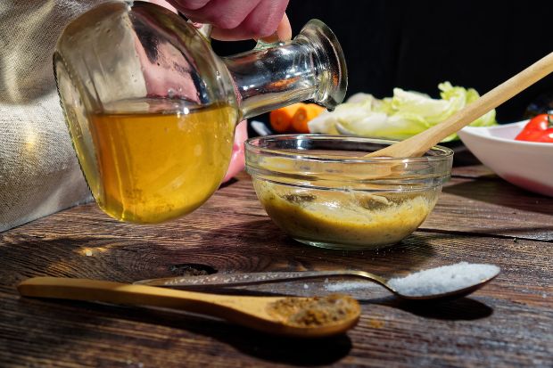 Cook pouring oil into salad dressing after learning how to keep homemade salad dressing from solidifying