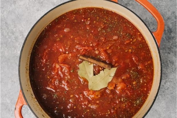 Pot of red sauce with two whole bay leaves in it instead of ground bay leaves