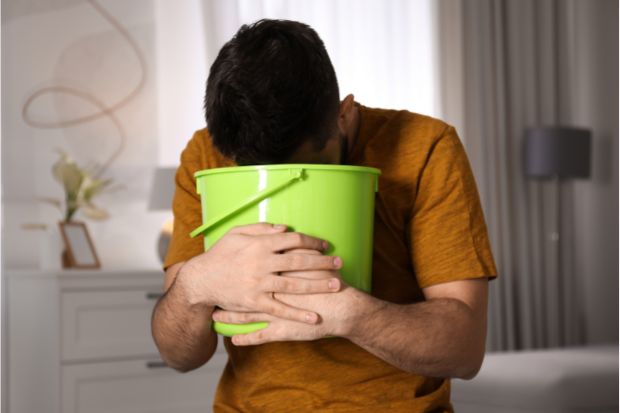 Man puking into green bucket after eating raw bacon