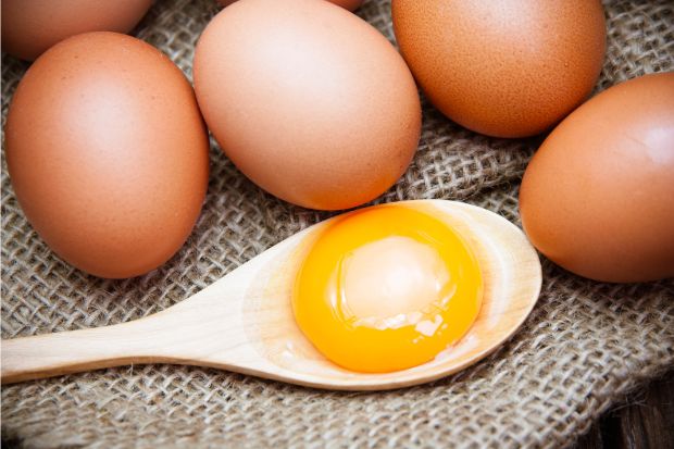 Egg yolk on a wooden spoon next to whole eggs