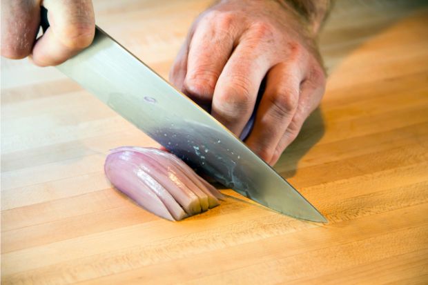 Chef using knife to slice shallot that will be used as a substitute for mushrooms in beef wellington