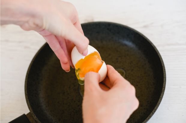 Cracking egg over frying pan with a yolk that breaks easily