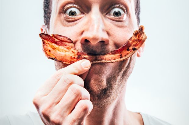 Man holding salty bacon strip up to his face like a smile