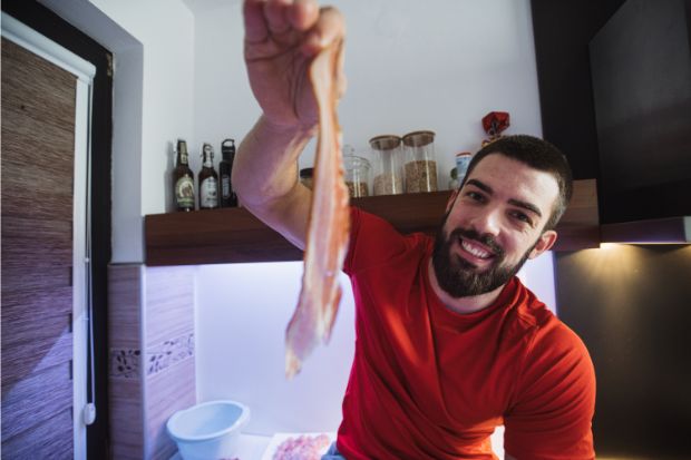 Man smiling and holding bacon that is very salty