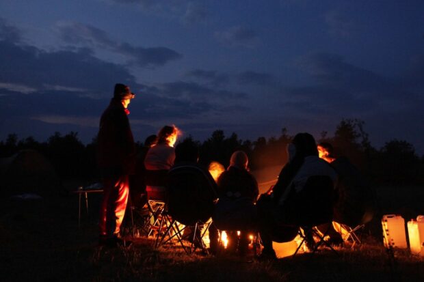 People sitting around campfire and toasting bagels without a toaster