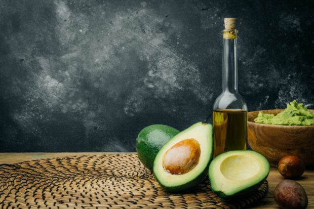 Bottle of avocado oil next to sliced avocados