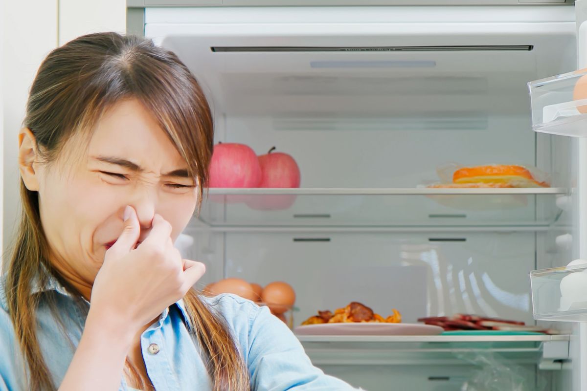 Woman plugging her nose because of garlic smell in fridge