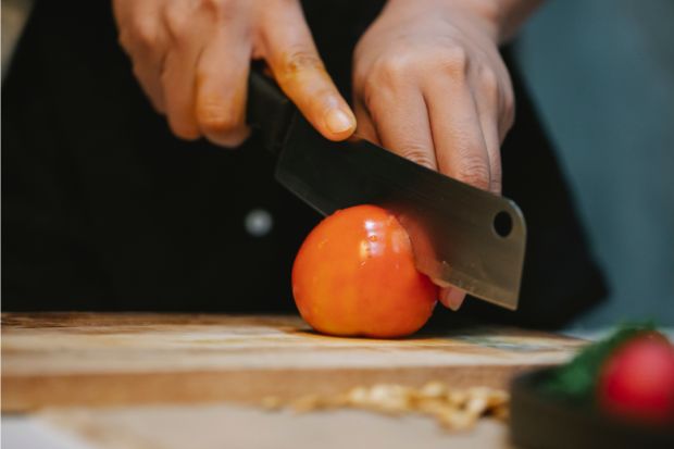 Pair of hands cutting a tomato with a chef's knife