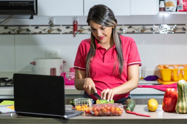 Woman cuts vegetables while watching YouTube on a laptop in her kitchen